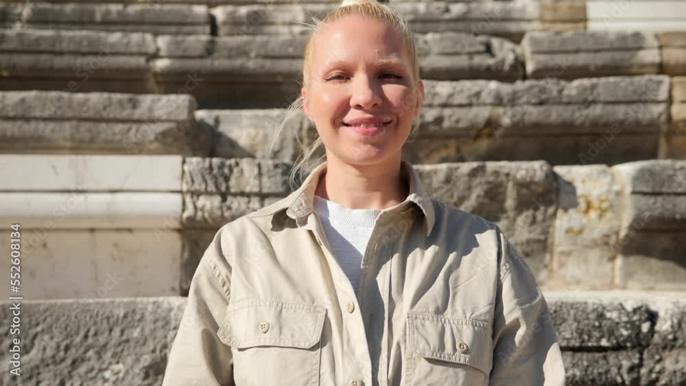 Portrait of a pretty young blonde woman with a smile looking at the camera on a sunny summer day. Portrait of an archaeologist against the background of the ancient steps of the amphitheater. 4k Portrait of a pretty young blonde woman with a smile looking at the camera on a sunny summer day. Portrait of an archaeologist against the background of the ancient steps of the amphitheater. 4k