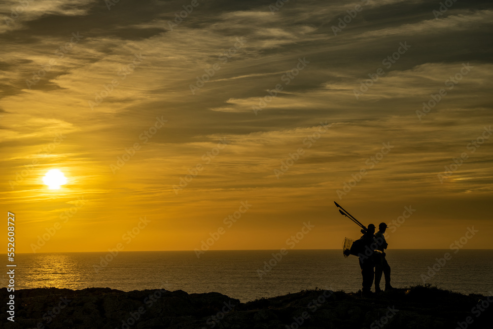 Czarna sylwetka rybaków stojących na klifie, pomarańczowy zachód słońca, przylądek Świętego Wincentego (port. Cabo de São Vicente) Portugalia - obrazy, fototapety, plakaty 