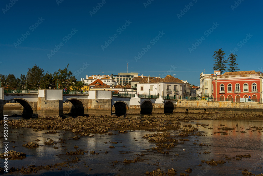 Widok na najstarszy most na rzece Gilao w miasteczku Tavira, Portugalia. Fragment nabrzeża, piękny słoneczny dzień. 