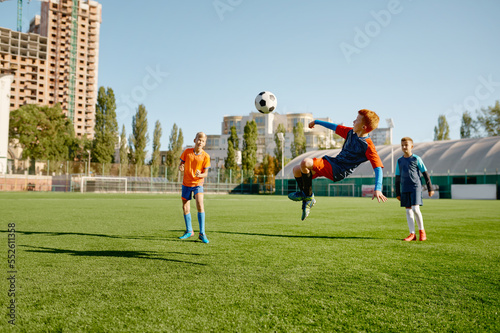 Junior forward jumping to kick ball with leg taking part in football match