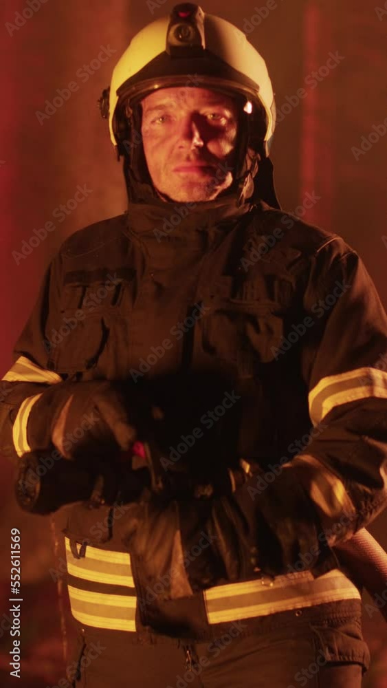 Vertical Screen: Portrait of a Brave Handsome Young Adult Firefighter in Safety Uniform and a Helmet Posing for Camera During a Wildfire. Professional Fireman Looking at Camera. Vertical Screen: Portrait of a Brave Handsome Young Adult Firefighter in Safety Uniform and a Helmet Posing for Camera During a Wildfire. Professional Fireman Looking at Camera.