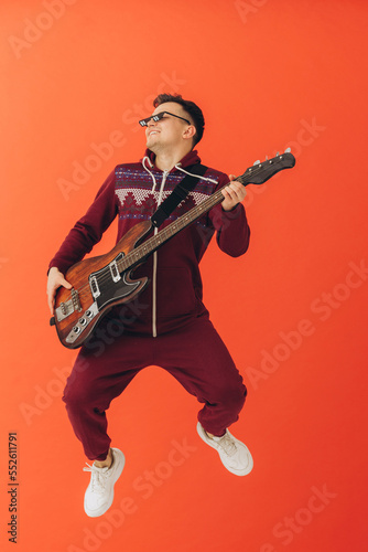 A young man in a Christmas kigurumi plays an electric guitar on a colored background.