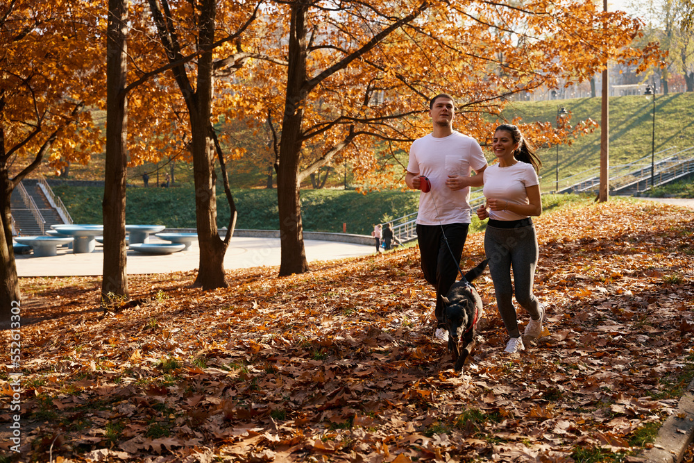 Cheerful young people run through fallen leaves with their dog Cheerful young people run through fallen leaves with their dog