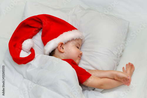 Little boy sleeping on white linen in the Santa hat.	