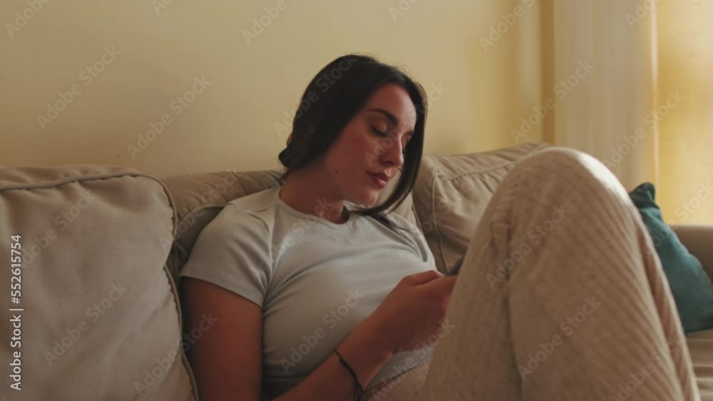 Young woman using mobile phone while sitting on sofa at home Young woman using mobile phone while sitting on sofa at home