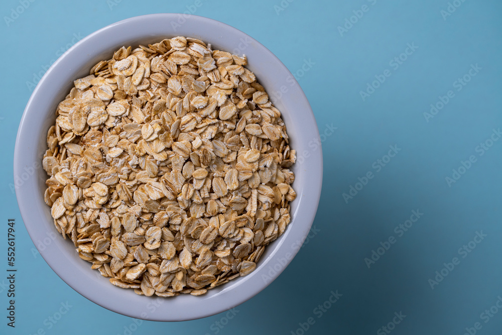 Dry oat flakes in a white plate on a blue background. Heap of oat flakes, top view, close up, copy space Dry oat flakes in a white plate on a blue background. Heap of oat flakes, top view, close up, copy space