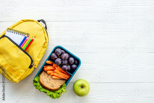 School lunchbox with fruits and yellow backpack, top view photo