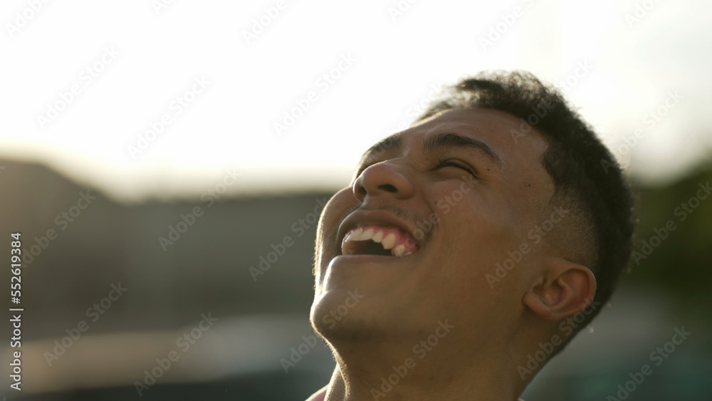 One ecstatic young hispanic man turning head to sky smiling with Hope and faith. Charismatic latin person laughing and feeling joy