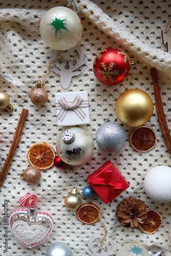 Various colorful Christmas ornaments, small presents and seasonal spices on white knitted blanket. Top view.