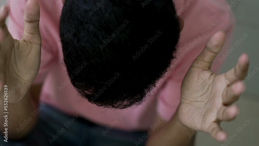 Fototapeta premium Evangelical young Brazilian man raising hands up while head bows down in reverence praising the lord. South American person worshiping God