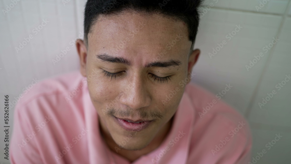 Obraz premium Evangelical young Brazilian man raising hands up while head bows down in reverence praising the lord. South American person worshiping God