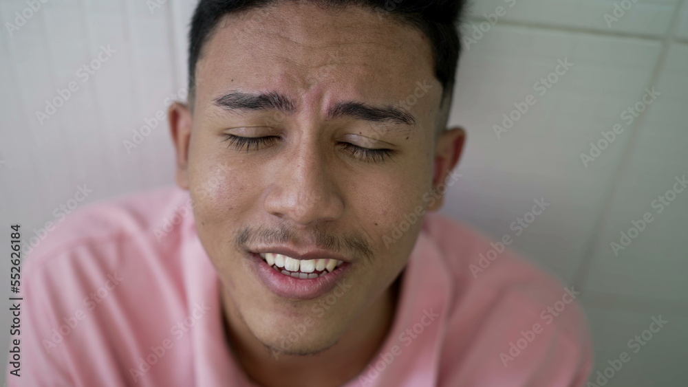Fototapeta premium Evangelical young Brazilian man raising hands up while head bows down in reverence praising the lord. South American person worshiping God