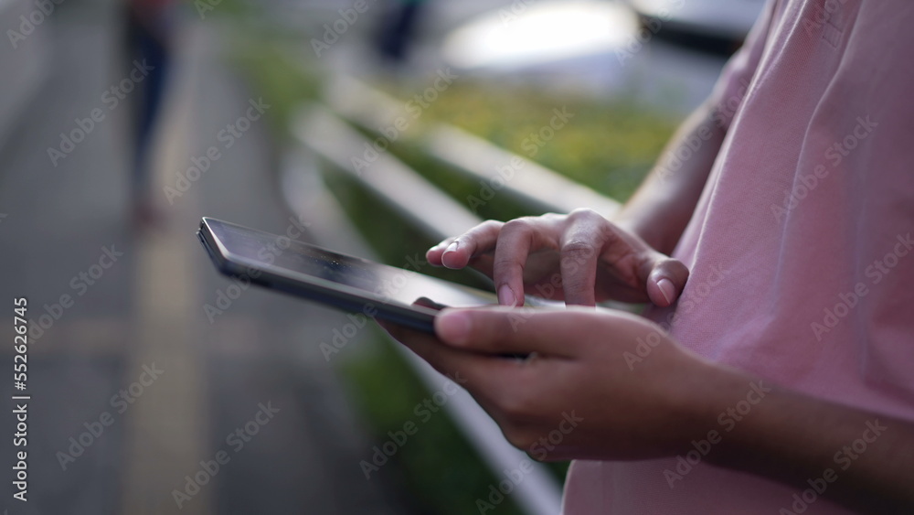 Closeup hand using tablet device outdoors. A hispanic person holding screen