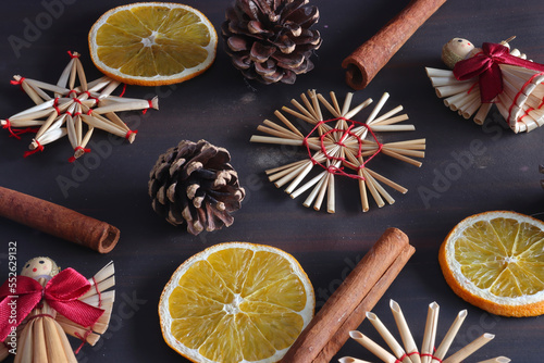 straw Christmas decorations in the shape of stars, snowflakes and angels, whole cinnamon sticks, cones from a tree and cut slices of dried oranges on a brown background