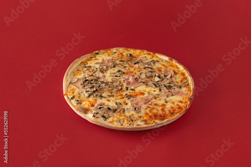 Whole tasty pizza standing on isolated dark red background. Minimal abstract concept of traditional Italian baked food. An idea for a restaurant or pizzeria card. A high-calorie fast food meal.