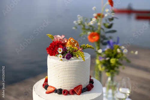 Billede på lærred wedding cake with berries and cream on the lakeshore with two glass of white win