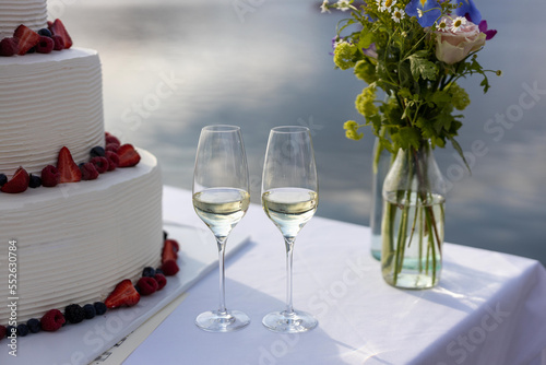 Billede på lærred wedding cake with berries and cream on the lakeshore with two glass of white win