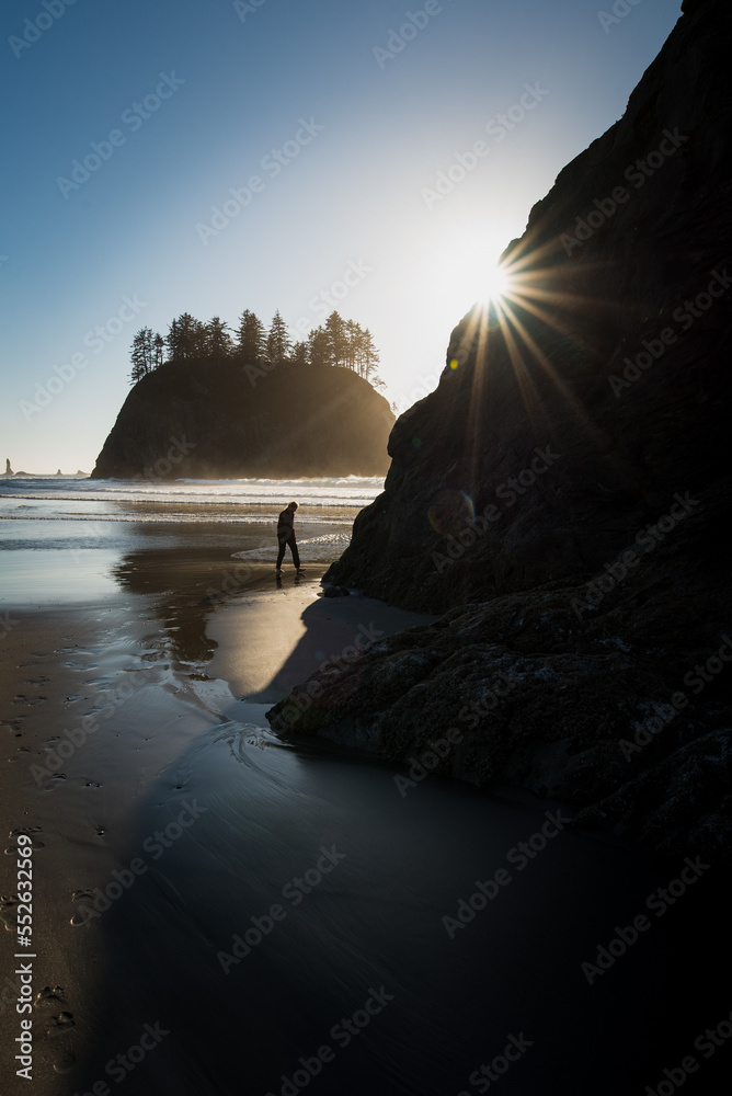 Afternoon sun behind sea stacks on Pacific Ocean with figure walking on dark sandy beach