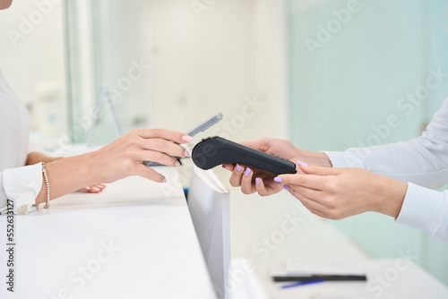 Female client making contactless payment at reception desk photo