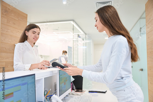 Smiling woman paying with smartphone at clinic reception desk