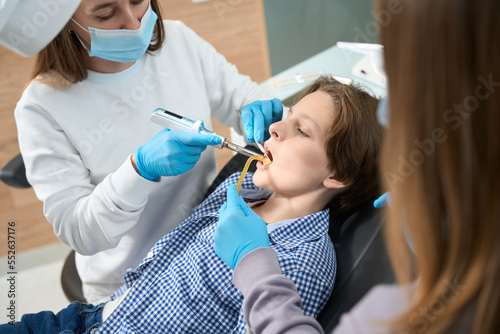 Woman dentist at the workplace treats tooth to a boy