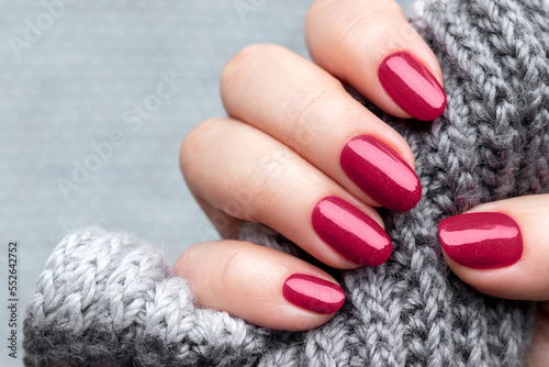 Female hand with knitted scarf and beautiful manicure - viva magenta, burgundy glittered nails