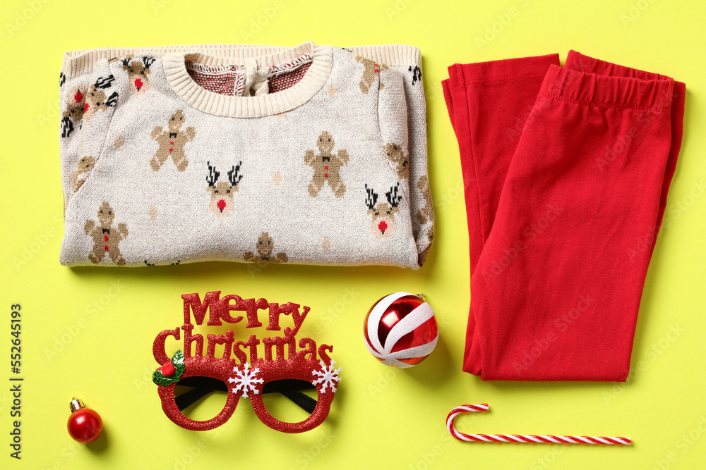Naklejka premium Set of Christmas baby clothes on color background. Flat lay festive jumper, pants, merry Christmas eyeglasses and decorations. Kids New Year outfit.