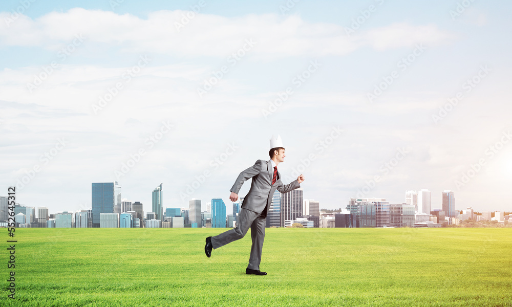 King businessman in elegant suit running on green grass and modern cityscape at background