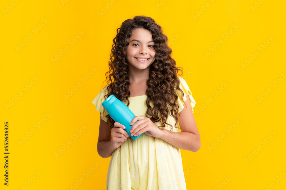Teenager child girl showing bottle shampoo conditioners or shower gel isolated on yellow background. Hair cosmetic product. Mock up bottle. Happy teenager portrait. Smiling girl. Teenager child girl showing bottle shampoo conditioners or shower gel isolated on yellow background. Hair cosmetic product. Mock up bottle. Happy teenager portrait. Smiling girl.