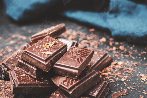Dark chocolate bar pieces on dark background with grated chocolate, pile chunks of broken chocolate