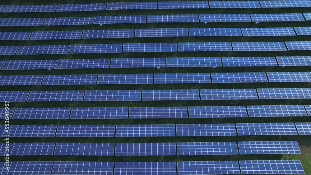 Aerial view of large photovoltaic solar farm on field during blue sky and sunlight - field farm in background. There is sunlight reflecting on the receiving panel. Aerial view of large photovoltaic solar farm on field during blue sky and sunlight - field farm in background. There is sunlight reflecting on the receiving panel.