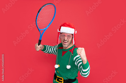 happy successful man in elf costume and santa claus hat. xmas guy hold tennis rocket © Olena