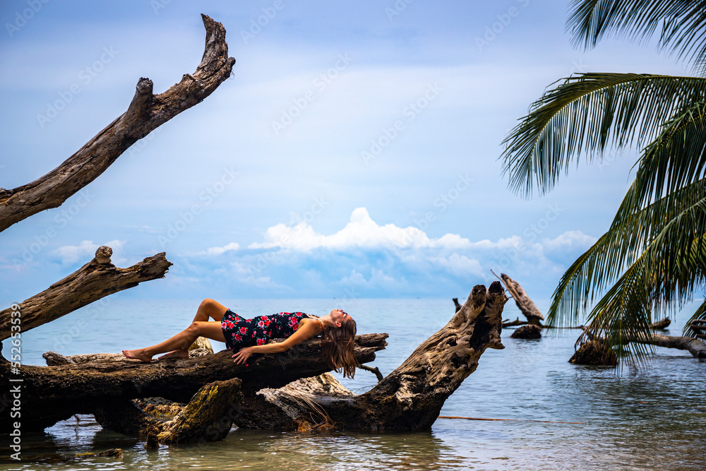 Relaxed girl in a dress lies on a tree trunk on a paradise beach in Costa Rica; relaxing on a tropical beach by the Caribbean sea