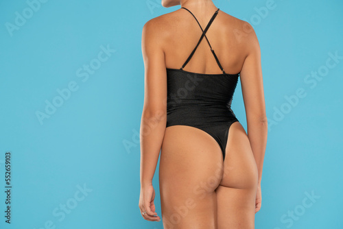 Torso of a  young woman in black monokini on a blue background, Back rear view. photo