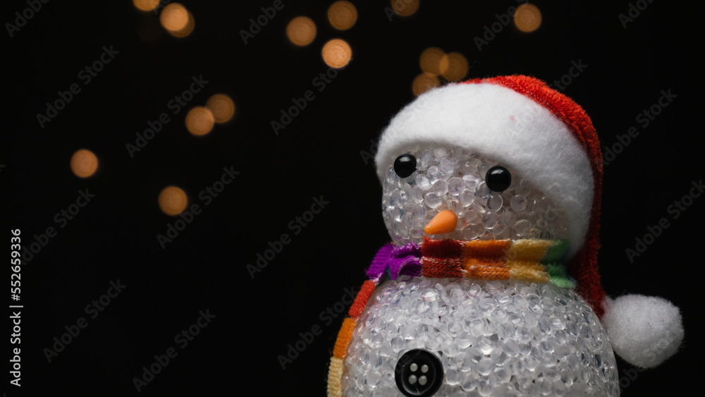 Obraz premium Figurine of snowman with Santa Claus hat on black background with orange bokeh lights