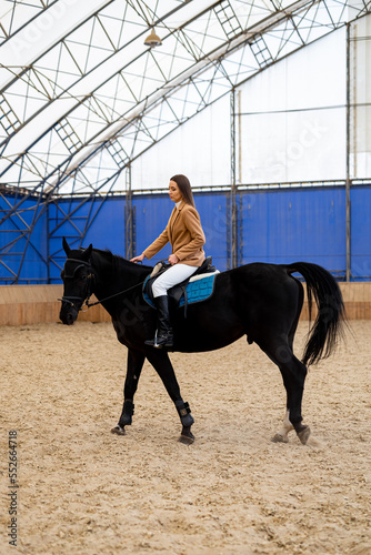 Pretty lady horse riding indoor. Elegant young woman in jockey uniform.