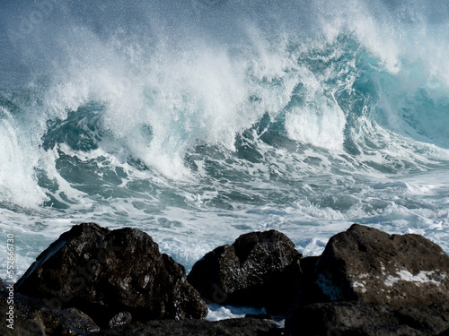 Fototapeta Naklejka Na Ścianę i Meble -  View of blue rolling wave slamming on volcanic rocks of the coastline like a tsunami. Beautiful spray due to the wind. Costa Teguise, Lanzarote, Canary Islands, Spain.