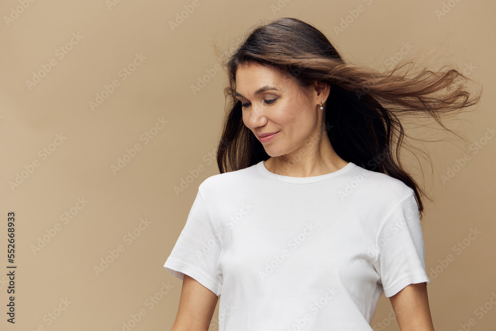 Obraz premium a beautiful cute attractive woman stands on a beige background with long hair developing in the wind, looking to the side with her head down.
