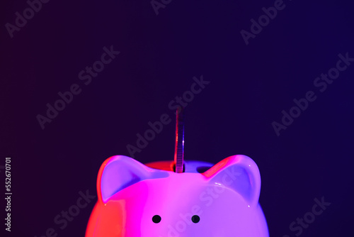 Piggy bank on a dark background with coin and red-purple backlight. Banking concept. Bright neon lights photo