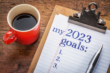 my 2023 goals list on clipboard and coffee against grunge wood desk, setting New Year goals and resolutions
