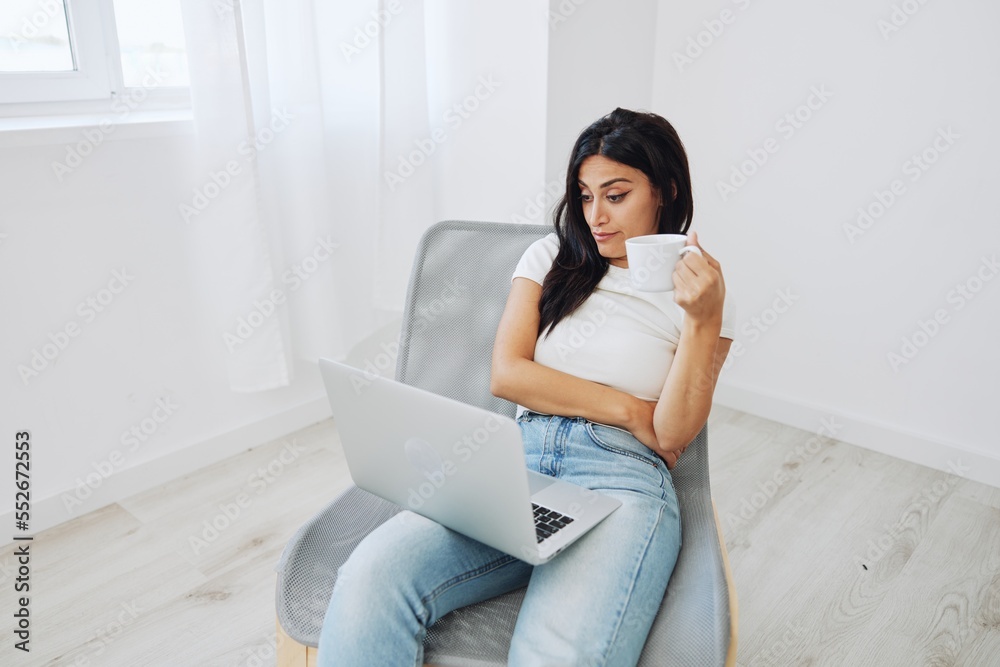 Woman relaxing at home sitting on a chair and watching a movie on her laptop with a cup of tea, autumn mood