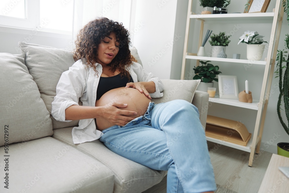 Pregnant woman smile and happiness lies on the couch freedom and strokes her belly with a baby in the last month of pregnancy, mother's day lifestyle