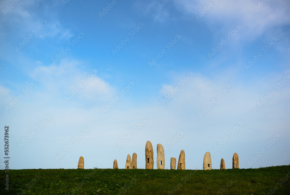 Stone dolmens with windows on a green meadow against a blue sky with clouds