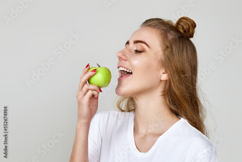 beautiful woman eating green apple on gray background.