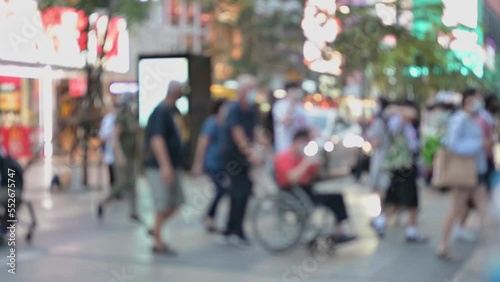 blur People and shoppers cross a busy city street. workers and traffic in a busy thailand city at night. blurry Person who uses a wheelchair, crosswalk street road. A officer directs traffic.