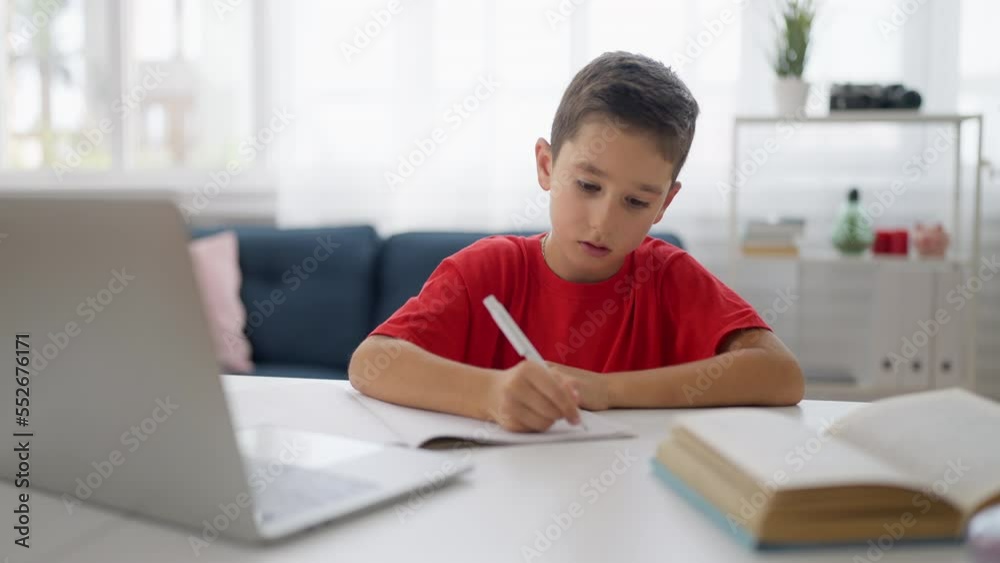 Focused boy doing homework at home, writing in notebook, homeschooling Focused boy doing homework at home, writing in notebook, homeschooling