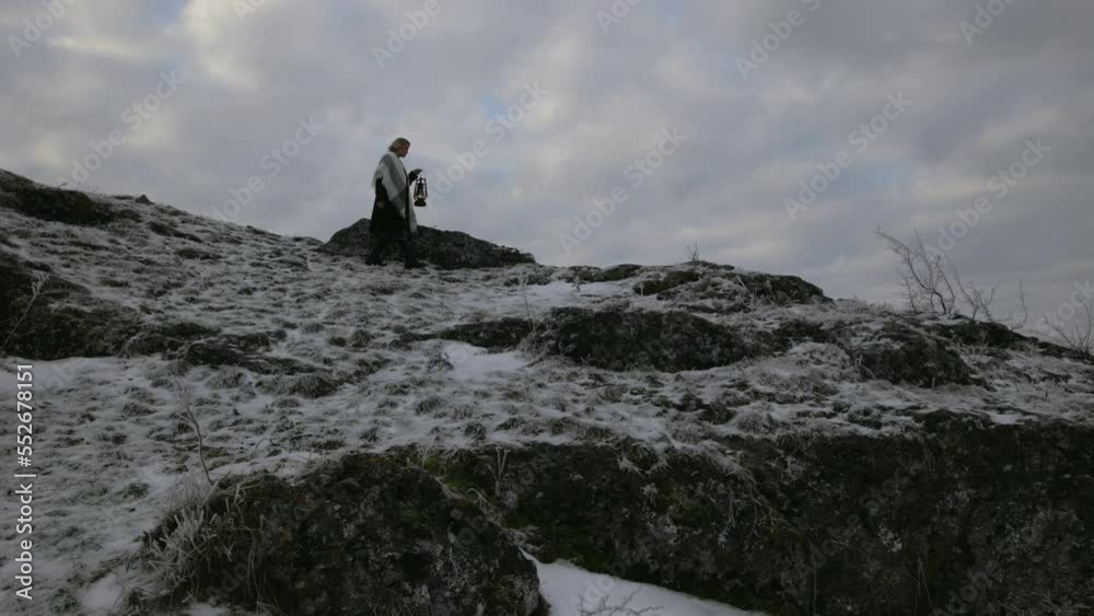 a woman with a lantern and a candle in her hands walks alone on the hillside, approaches the edge of the rock and stops, gray winter evening, snowy, atmosphere of a Christmas fairy tale, mystical mood a woman with a lantern and a candle in her hands walks alone on the hillside, approaches the edge of the rock and stops, gray winter evening, snowy, atmosphere of a Christmas fairy tale, mystical mood