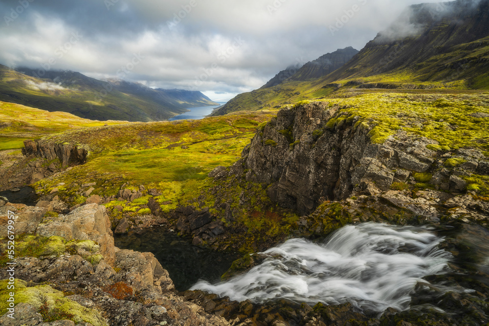 Rugged Icelandic landscape with bright green tundra and a view of the coastline in the distance; Iceland Rugged Icelandic landscape with bright green tundra and a view of the coastline in the distance; Iceland