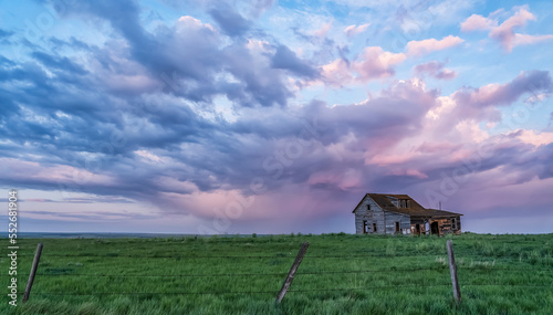 Old farmstead on the prairies under glowing storm clouds at sunset; Val Marie, Alberta, Canada photo