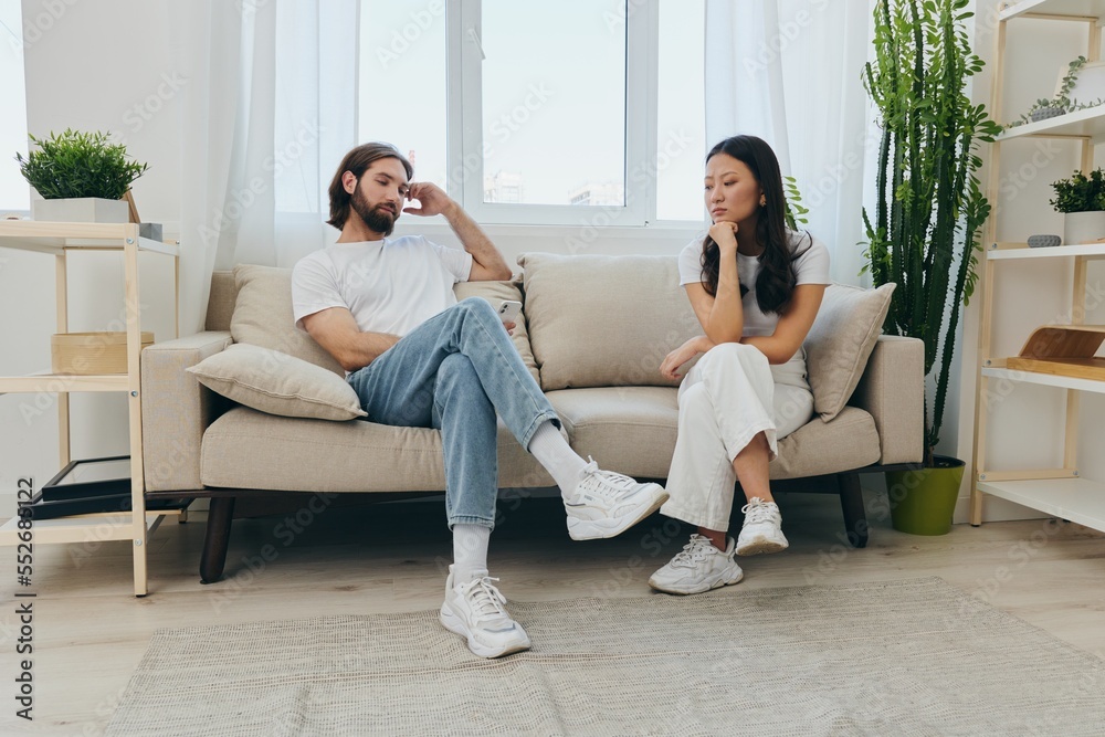 A young married couple sitting on the couch not talking to each other, family quarrels and discontent. Lifestyle in misunderstanding and unwillingness to work on the relationship for love A young married couple sitting on the couch not talking to each other, family quarrels and discontent. Lifestyle in misunderstanding and unwillingness to work on the relationship for love